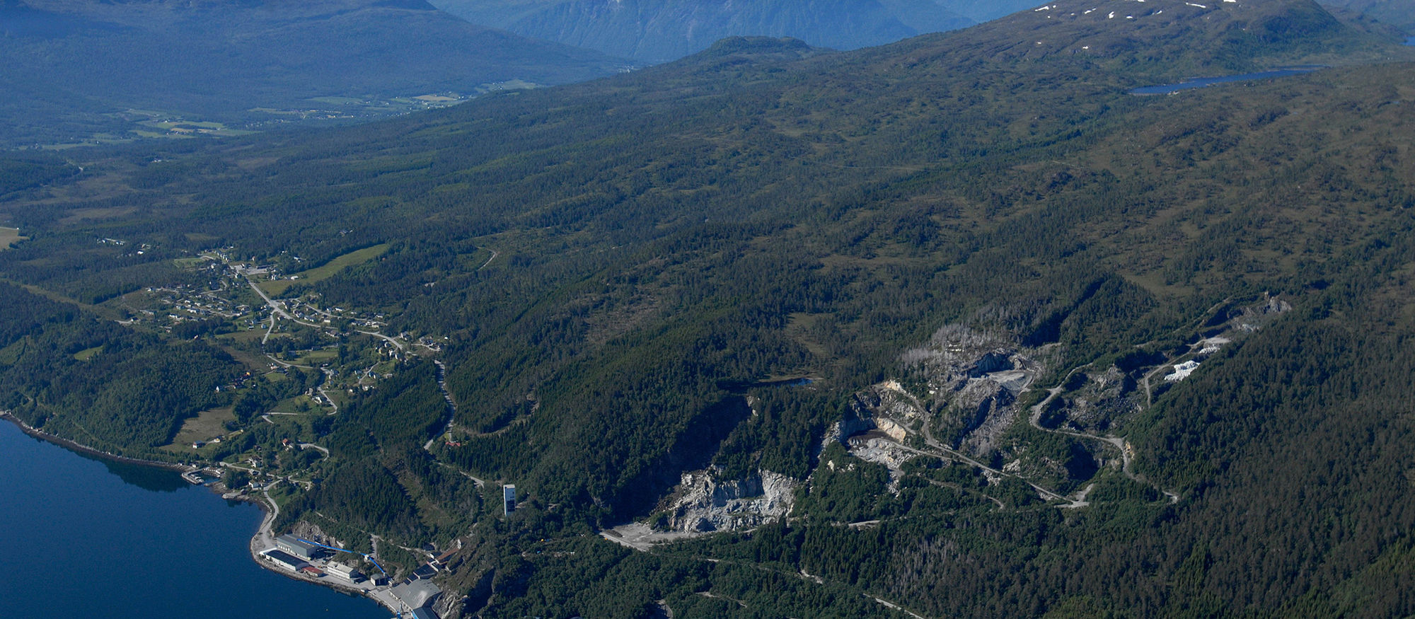 Flyfoto med utsikt over fjord og fjell. Massemottak i åsside. Foto.